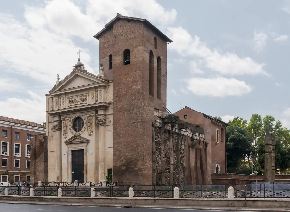 Den lyse barokfacade på San Nicola in Carcere ved siden af det høje murede middelalderlige klokketårn under en overskyet himmel