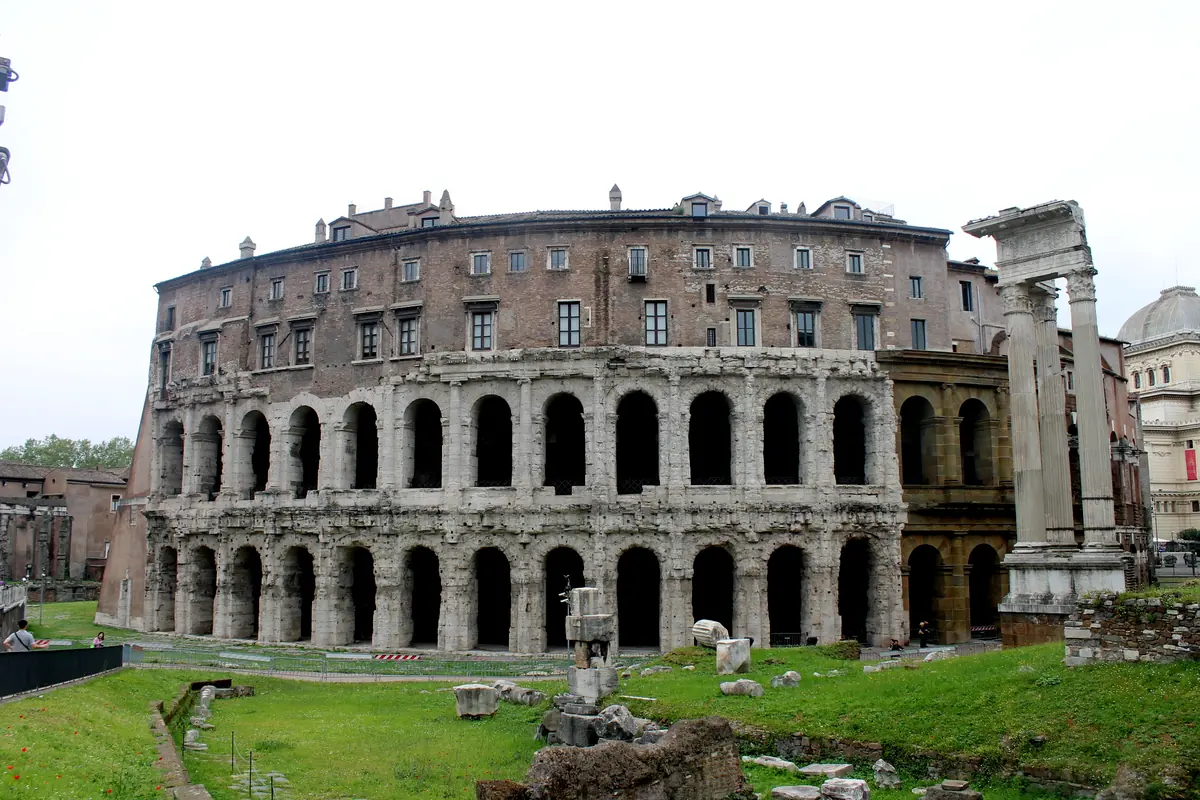 Den buede facade på Theatre of Marcellus i Rom: to etager af antikke buer med en senere palazzosetage ovenover og tre stående søjler fra et tempel til højre